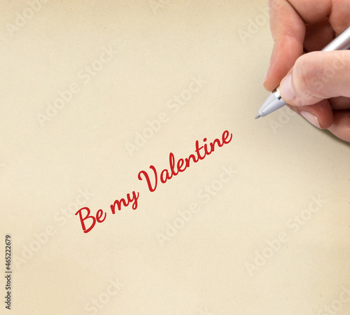 Hand writing "Be my Valentine" on yellow sheet of paper.