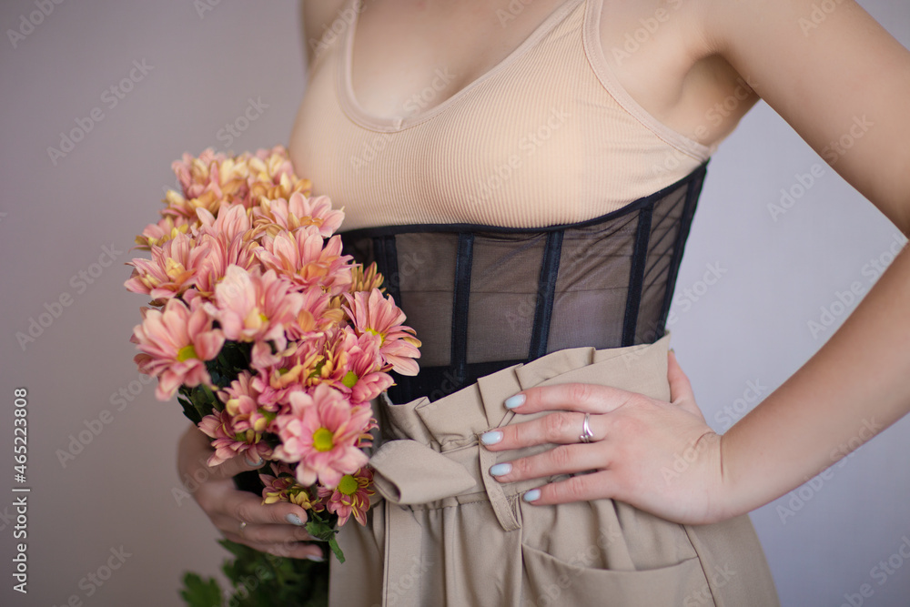 girl in a beige top, corset and trousers and holding flowers in her hands