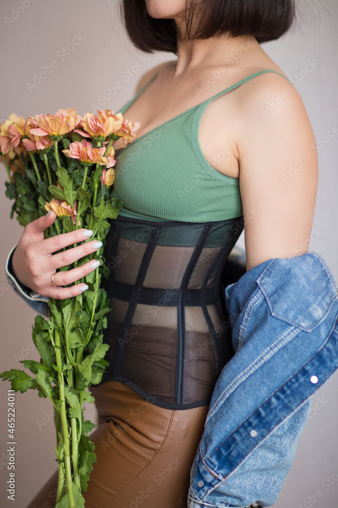 a girl in a green top, corset, leather pants and a denim jacket holds flowers in her hands