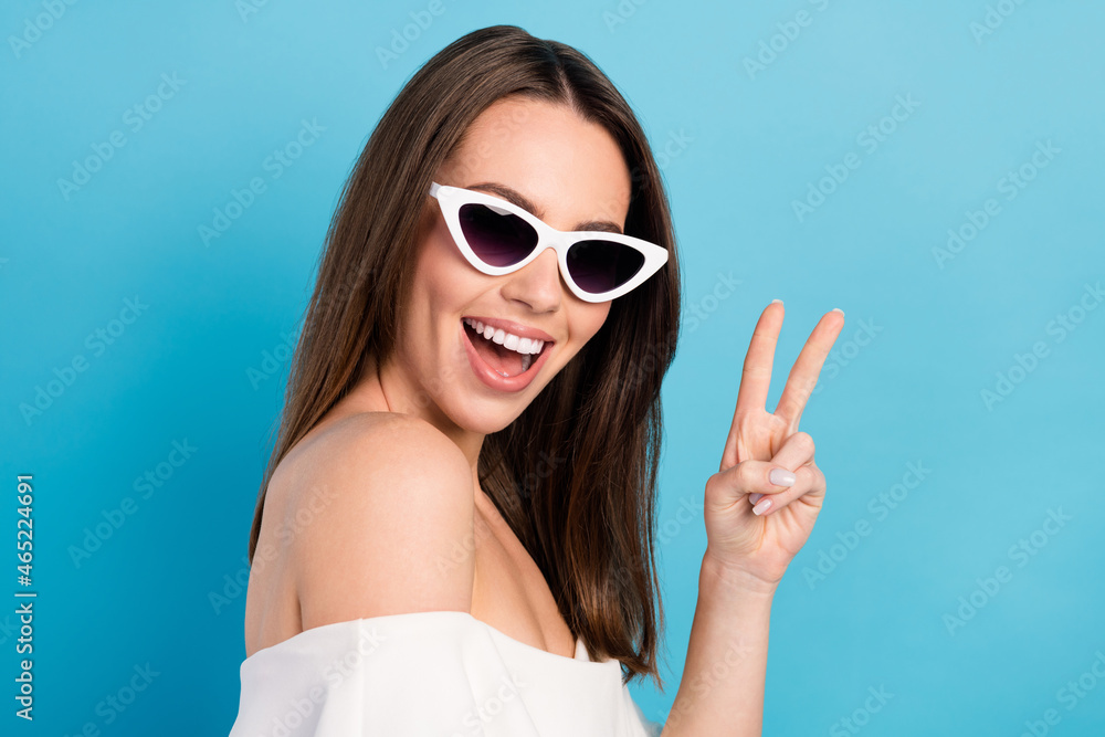 Photo of charming pretty young lady wear off-shoulders shirt dark eyewear smiling showing v-sign isolated blue color background Photo of charming pretty young lady wear off-shoulders shirt dark eyewear smiling showing v-sign isolated blue color background