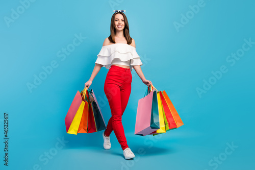 Full length photo of happy pretty charming woman walk hold hands shopping bags isolated on blue color background