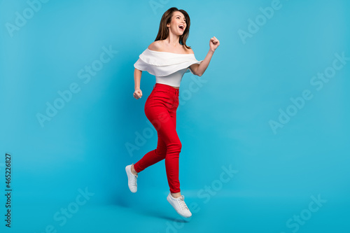 Photo of impressed funky woman dressed white blouse smiling jumping running looking empty space isolated blue color background