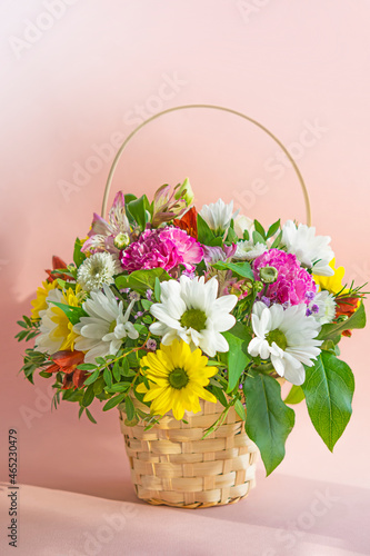 A basket with a bouquet of flowers. Roses and chrysanthemums in a basket on a pink background. A gift for Valentine's day, birthday