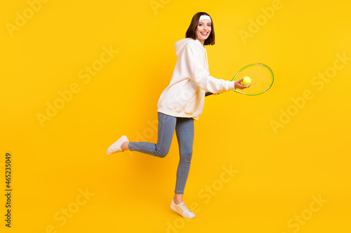 Photo of cheerful sportswoman hold racket ball wear headband hoodie jeans shoes isolated yellow color background © deagreez