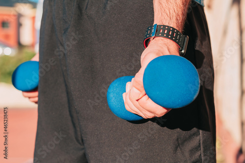 Close up shot of the hands of a sportsman holding weights with a smart whatch on his wrist while training outdoors. Sports and gym equipment concept. photo
