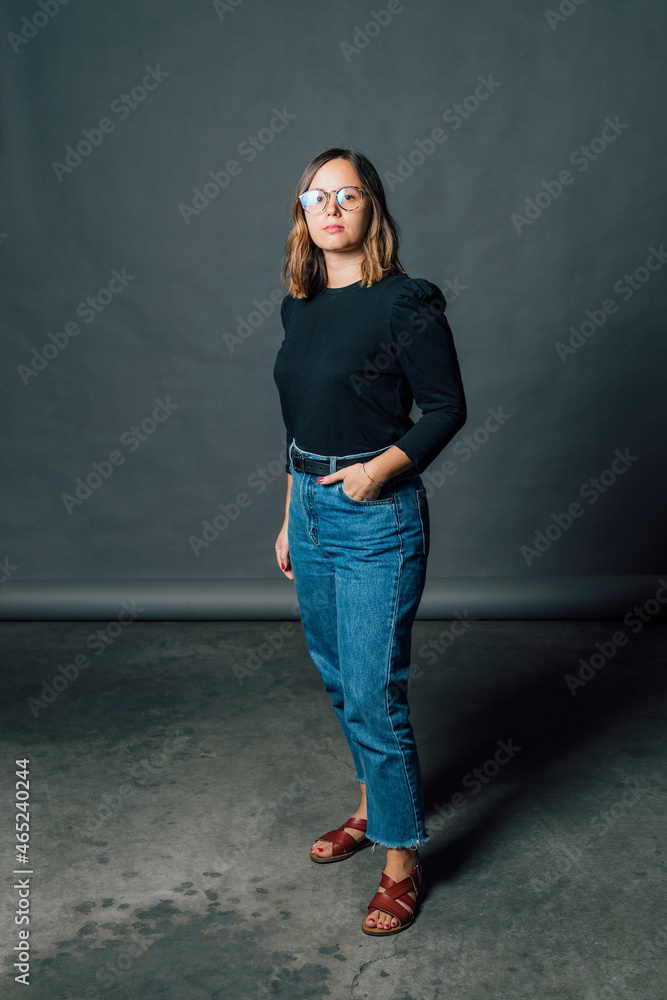 Confident woman with hand in pocket standing in front of gray backdrop Confident woman with hand in pocket standing in front of gray backdrop
