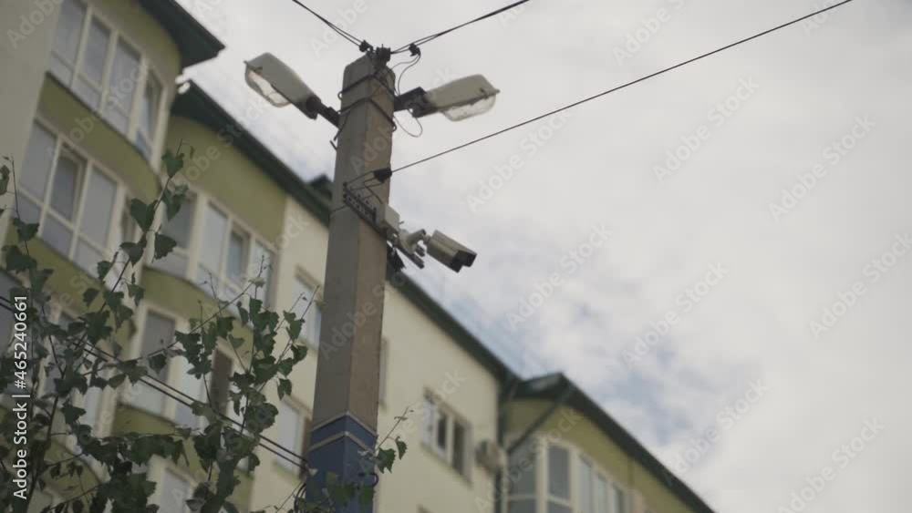 Security camera hanging on the utility pole in the yard of the apartment block. Safety of residents of the city. Close up video of the video surveillance system near the multi-story apartment building Security camera hanging on the utility pole in the yard of the apartment block. Safety of residents of the city. Close up video of the video surveillance system near the multi-story apartment building