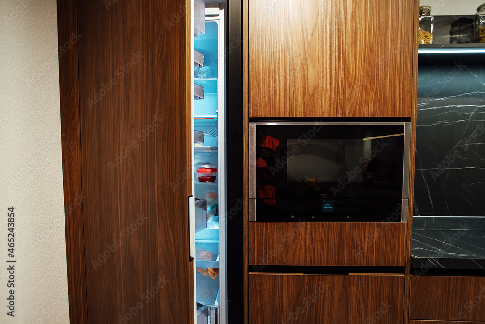 an open refrigerator door in the kitchen in a minimalist design. strict brown kitchen facade. expensive apartment interior an open refrigerator door in the kitchen in a minimalist design. strict brown kitchen facade. expensive apartment interior