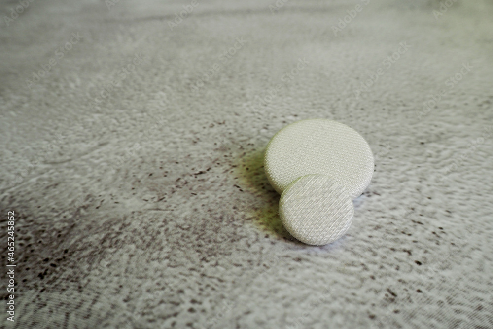 two white fabric buttons of different sizes lie on a gray background. side view two white fabric buttons of different sizes lie on a gray background. side view