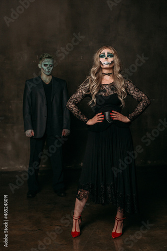 The image of a skeleton girl and the image of a Frankenstein man on Halloween in the dark. an image for a couple on Halloween. a woman stands in the foreground in a black lace dress