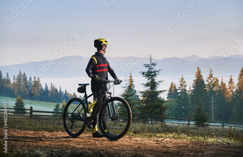 Fototapeta Naklejka Na Ścianę i Meble -  Male cyclist standing with bike with coniferous trees and hills on background. Man bicyclist enjoying bicycle ride in mountains in the morning. Concept of sport, biking and active leisure.