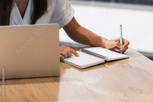 Female professional with laptop writing in diary at restaurant photo
