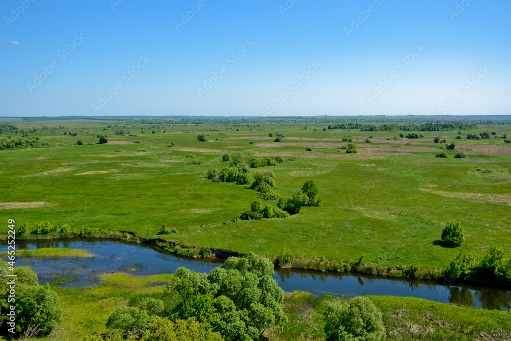 Green field with river and blue sky on a sunny summer day. Horizontal photo of a rural landscape
