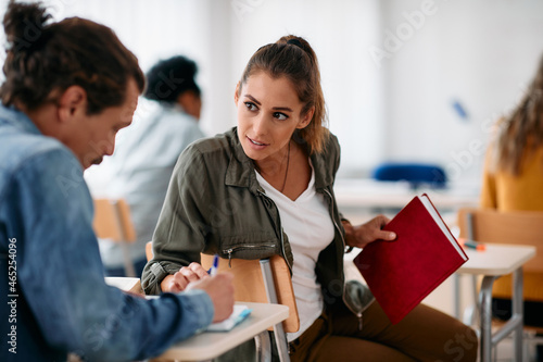 Young student communicates with her friend during lecture in classroom.