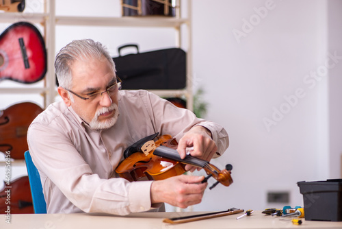 Obraz na plátně Old male repairman repairing musical instruments at workplace