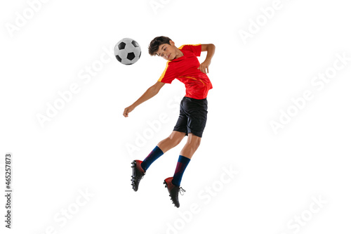 Portrait of boy, teenager, professional football player in motion, kincking a ball with head isolated over white background photo