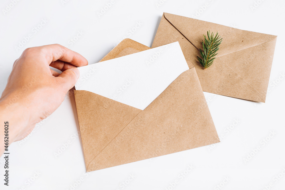 Hand holding christmas blank greeting card mock up. Craft envelope, pine twig and card template with empty space for holiday message on white background. Happy new year minimal composition Hand holding christmas blank greeting card mock up. Craft envelope, pine twig and card template with empty space for holiday message on white background. Happy new year minimal composition