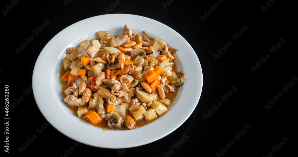 A traditional Chinese dish of chicken stew, with almonds, carrots and pasta. In a plate on a black background, close-up. A traditional Chinese dish of chicken stew, with almonds, carrots and pasta. In a plate on a black background, close-up.
