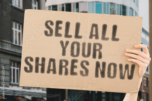 The phrase   Sell all your shares now   drawn on a carton banner in men s hand. Human holds a cardboard with an inscription. Crisis. Deal. Dollar. Drop. Expertise. Falling. Interest. Panic. Security