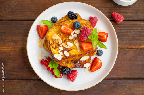 A stack of French toast on a plate with fresh berries, almond petals and honey on a dark wooden background. Delicious breakfast. Copy space.