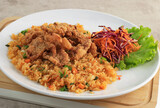 Nasi Goreng with Crispy Chicken SKin Topping, Served with Shredded Fresh Carrot and Purple Cabbage. On White Plate, Brown Table.