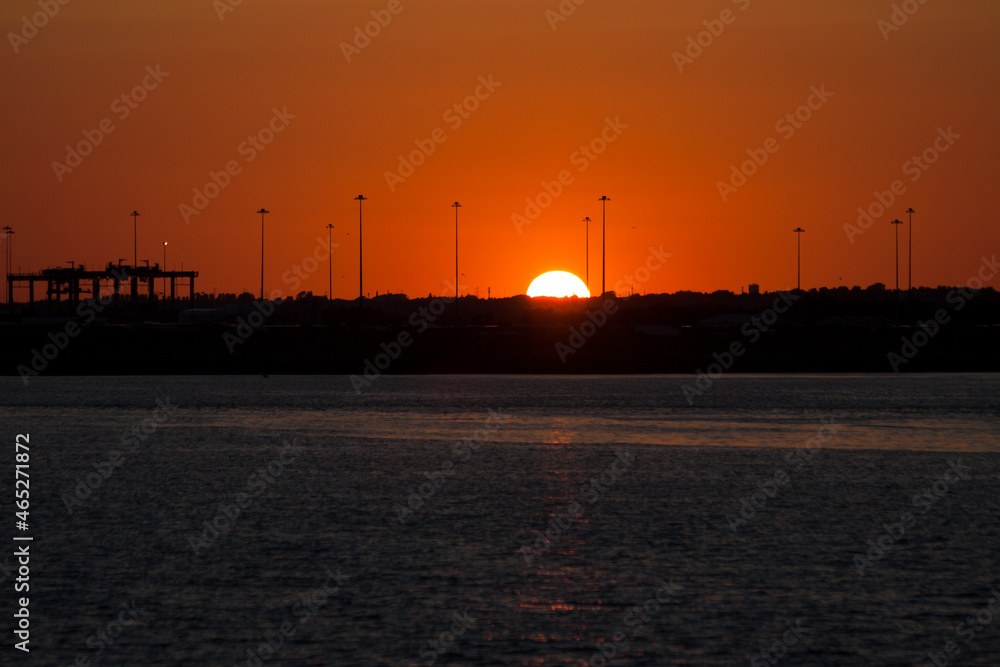 Sunset at Dublin Port with silhouettes of port cranes and lamp posts 