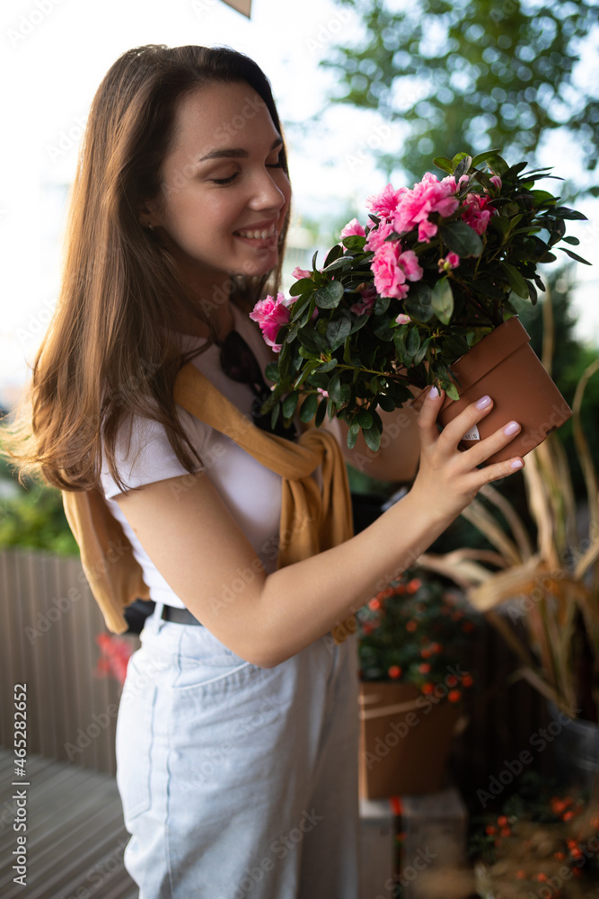 happy caucasian young woman chooses potted flowers to buy at outdoor garden stall