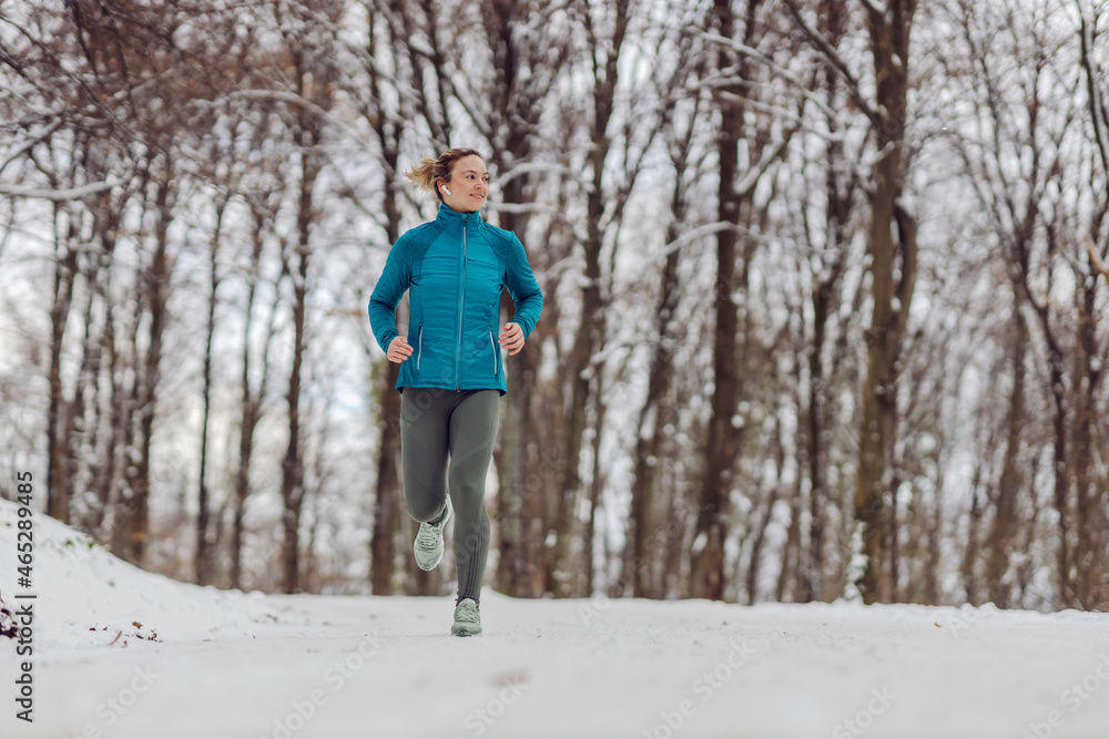 Slim sportswoman running in forest on a snowy weather. Cold weather, snow, healthy life, fitness, healthy habits, nature