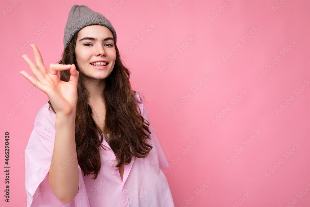 Photo of young positive happy smiling beautiful woman with sincere emotions wearing stylish clothes isolated over background with copy space and showing okay gesture demonstrating agreement Photo of young positive happy smiling beautiful woman with sincere emotions wearing stylish clothes isolated over background with copy space and showing okay gesture demonstrating agreement
