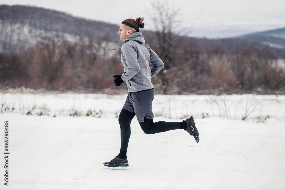 Sportsman running in nature at snowy winter day. Healthy habits, outdoor fitness, marathon