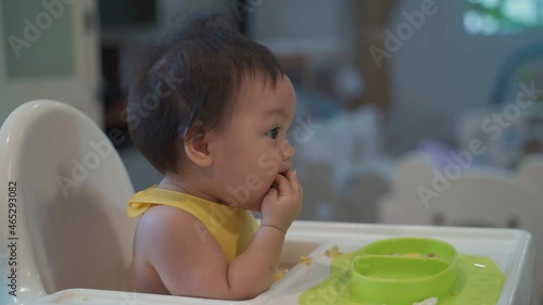 asian infant eating by hands, Baby eating with BLW method, baby led weaning. Happy kid enjoy food. Toddler self-feeding. infant baby eating. authentic life at home. baby chair hand feeding table.