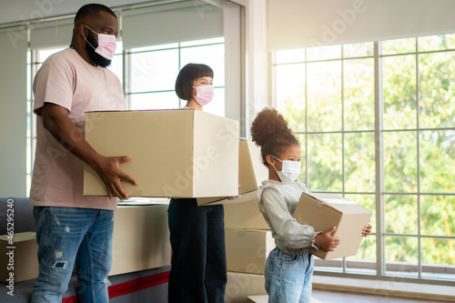 Mixed Race families are carrying cardboard boxes and walking from the front door into the house in a new house on moving day. Concept of relocation, rental, and homeowner moving at home. © Prot