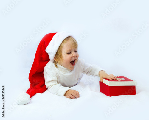 A happy child in a Santa Claus hat lies on a light background and rejoices at the gift. The concept of New Year and Christmas. place for text, flyer, advertisement