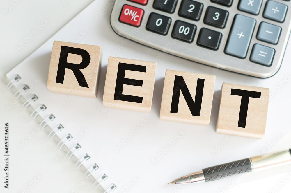 Wooden cubes with the word text RENT on white notebook next to a pen and a calculator on the table Wooden cubes with the word text RENT on white notebook next to a pen and a calculator on the table