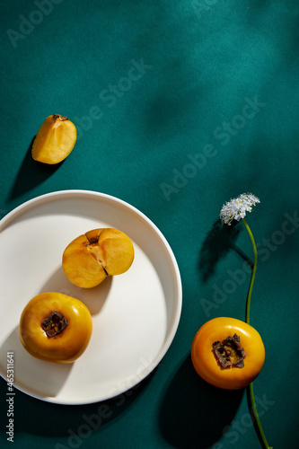 Top view of persimmon in white plate , flower with blue background for advertising 