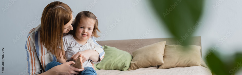Woman hugging toddler daughter with down syndrome on bed, banner. Woman hugging toddler daughter with down syndrome on bed, banner.