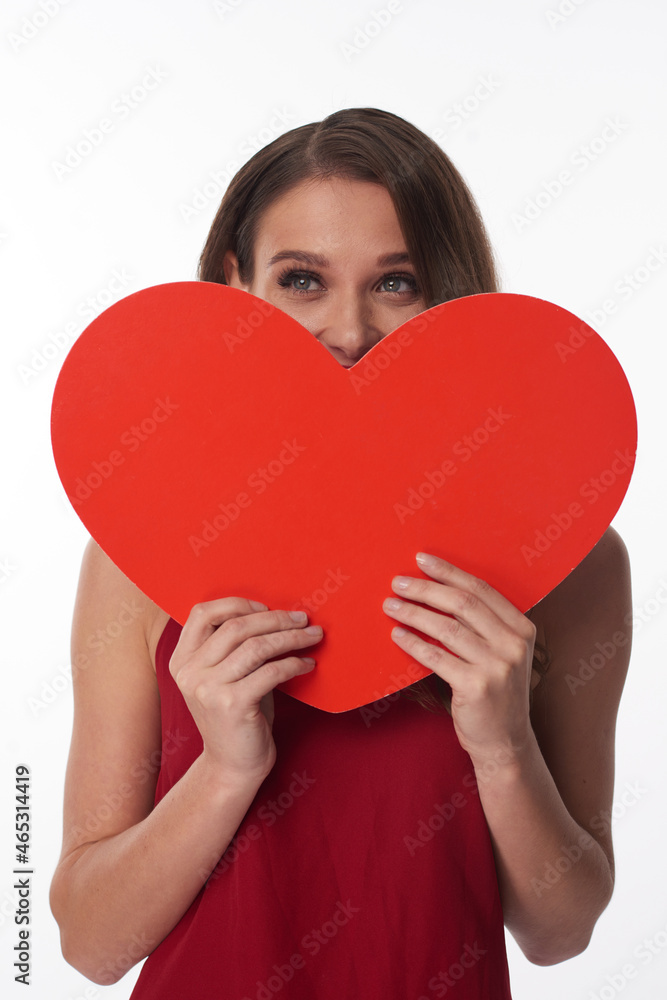Dreamy pretty young Caucasian woman falling in love covering mouth behind heart-shaped sign Dreamy pretty young Caucasian woman falling in love covering mouth behind heart-shaped sign