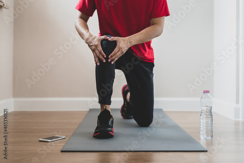 Young athletes wearing red t-shirt with water bottle and smartphone have a right knee injury during intense workout at home. He sat down and stretched his muscles to improve the injury.