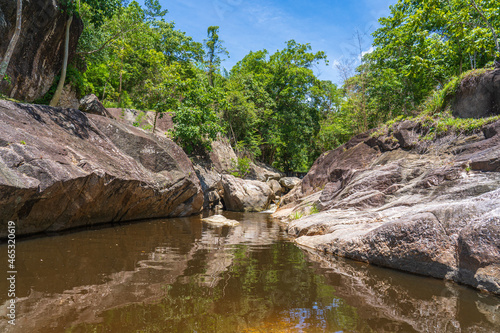 A small waterfall that flow through the boulders into a creek in a Thai national park on a clear day.