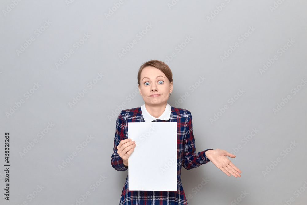 Confused woman is holding blank paper sheet and shrugging shoulders Confused woman is holding blank paper sheet and shrugging shoulders