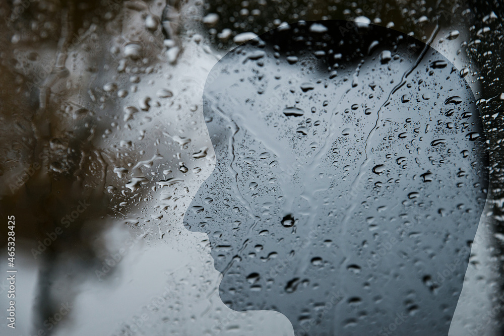 Silhouette of a human face behind a window with raindrops, dark, depression, loneliness, negative emotions Silhouette of a human face behind a window with raindrops, dark, depression, loneliness, negative emotions