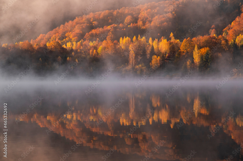 Sunrise with autumn colors on a foggy morning at the lake