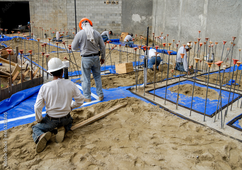 Workers installing synthetic waterproofing material as a vapor barrier under pending concrete