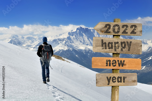 2020 happy new year wrtten on a postsign with a hiker walking on the snow in a mountain background photo