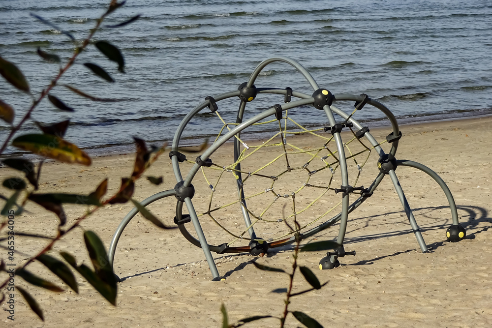 Empty kids playground for children on a sandy beach of the Baltic sea. Blurred branch with leaves in the front. Pirita, Tallinn, Estonia Empty kids playground for children on a sandy beach of the Baltic sea. Blurred branch with leaves in the front. Pirita, Tallinn, Estonia