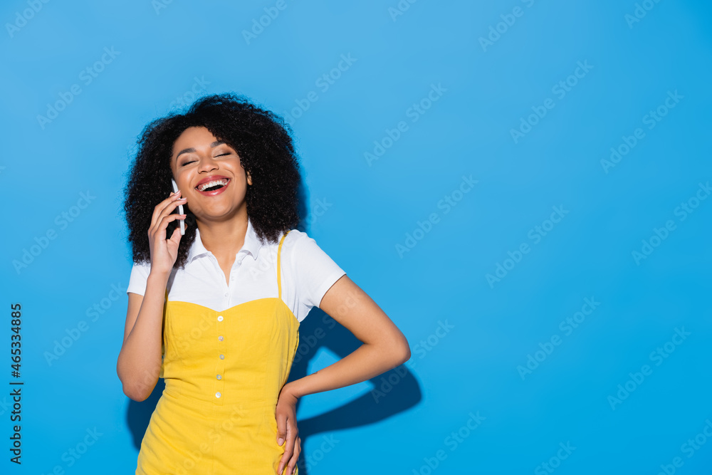 cheerful african american woman with closed eyes and hand on hip talking on smartphone on blue cheerful african american woman with closed eyes and hand on hip talking on smartphone on blue