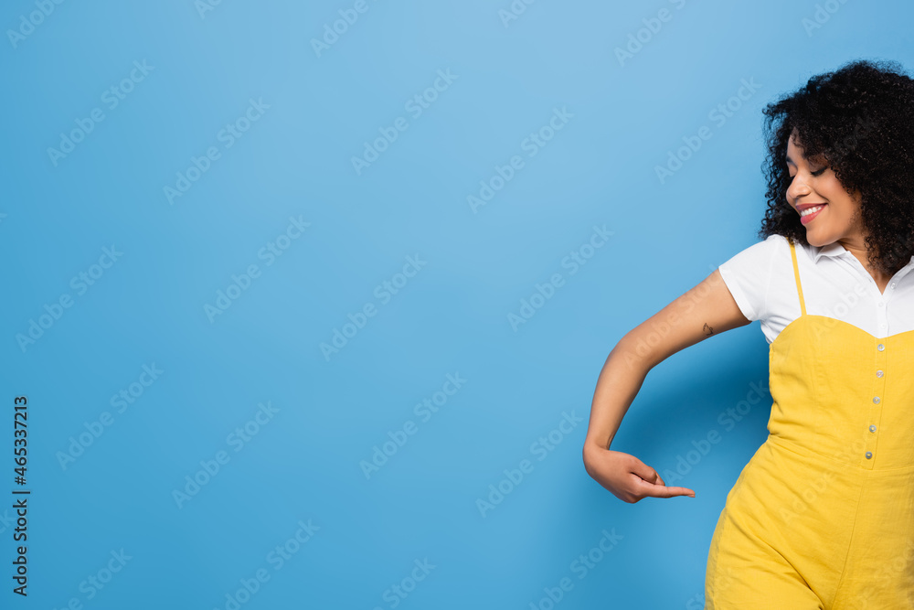happy african american woman pointing with finger at her hip on blue happy african american woman pointing with finger at her hip on blue