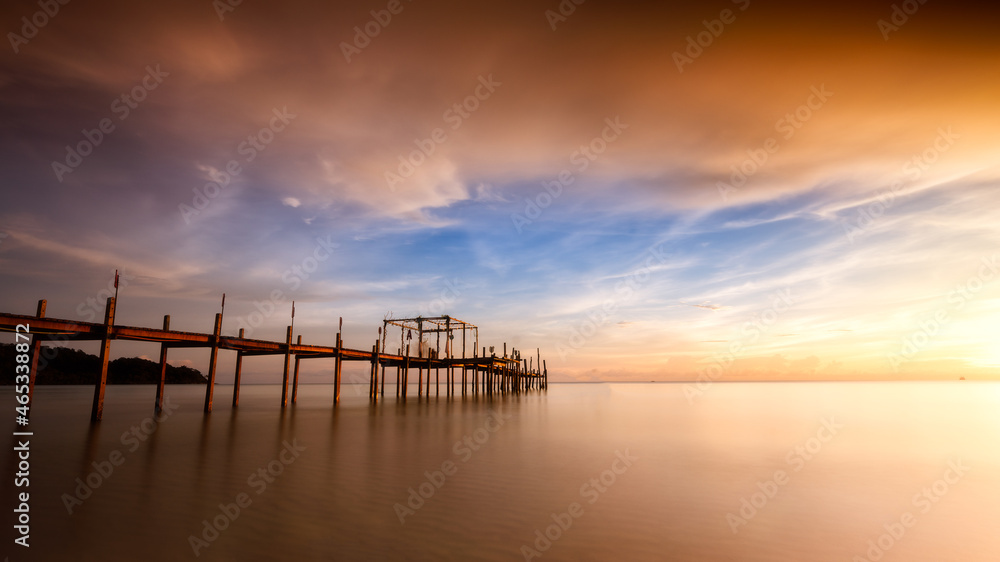 Long exposure shot of seascape with colorful twilight sky and wooden bridge.