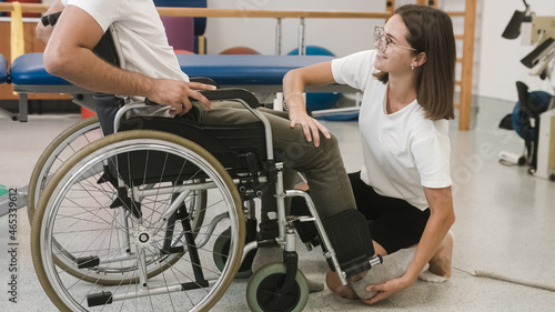 Female physiotherapist and male patient seated in a wheelchair during rehabilitation treatment - joint mobility, and strengthening of leg muscles