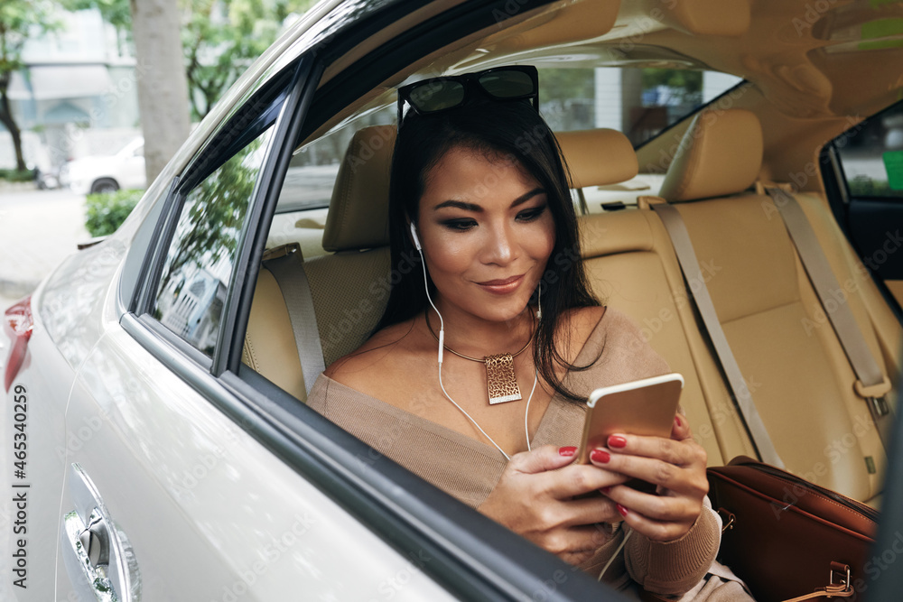 Naklejka premium Content elegant young Asian woman in earphones wearing sunglasses on head listening to music from phone